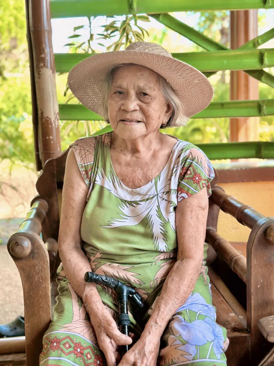 Cyril's grandmother seated outdoors wearing a sun hat